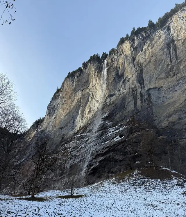 La chute du Staubbach sur la paroi rocheuse, au-dessus de la prairie enneigée de Lauterbrunnen