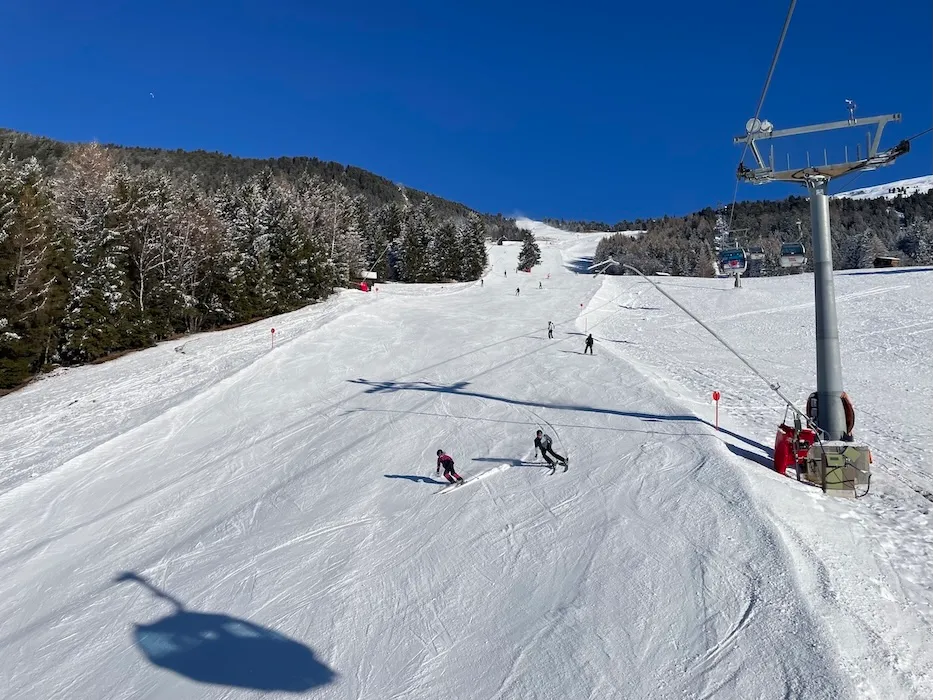 Skifahrer auf der Piste im Hochzeiger Skigebiet in Tirol mit Sessellift, verschneiten Hängen, Waldabschnitten und blauem Himmel an einem sonnigen Wintertag.