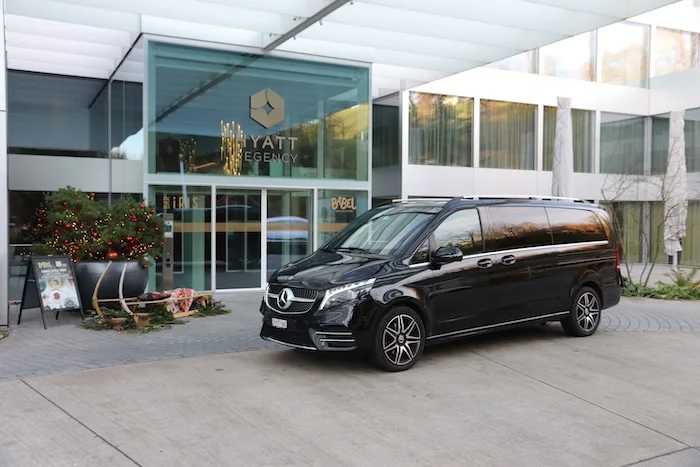 A black Mercedes-Benz van from a business chauffeur service in front of the entrance to the Hyatt Regency Hotel, ready for an exclusive transfer.