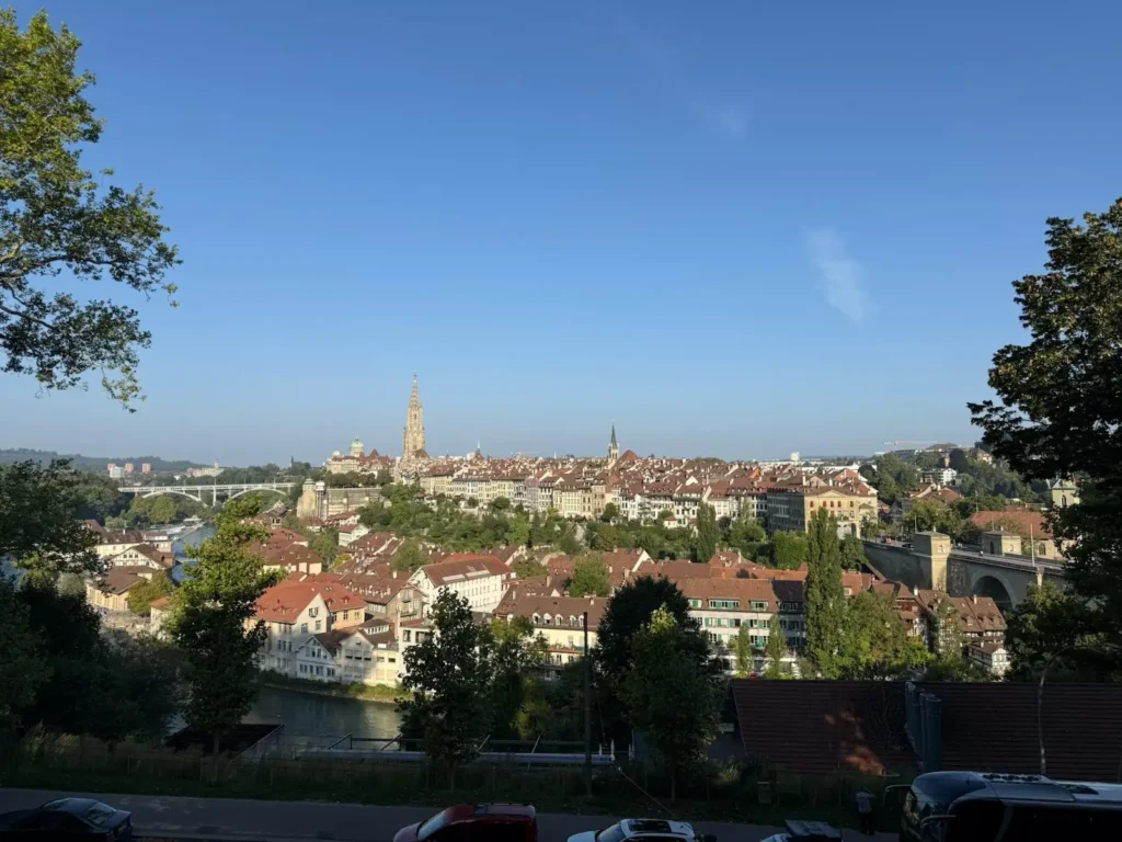 Transfer Zürich Bern: A view over the old town of Bern with the Münster tower and the turquoise-green loop of the Aare on a clear summer day.