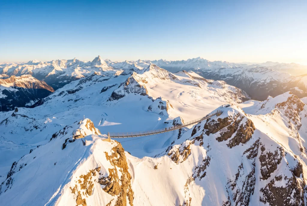Glacier 3000 Ausflug ab Zürich mit Chauffeur – die Peak-Walk-Hängebrücke zwischen zwei verschneiten Gipfeln am Scex Rouge, schneebedeckter Gletscher und ein weites Alpenpanorama bis zum Matterhorn im goldenen Abendlicht