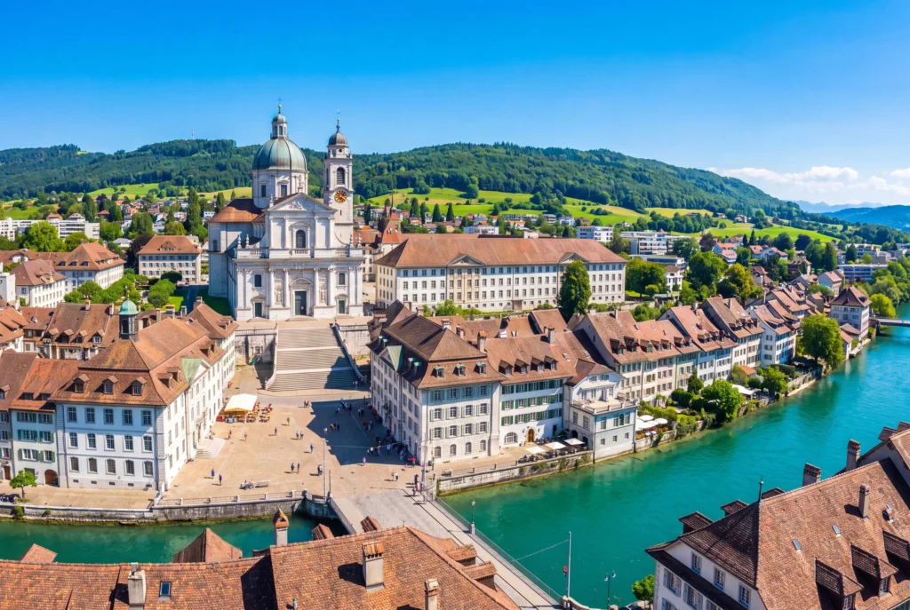 Solothurn Privattour ab Zürich mit Chauffeur – die weisse barocke St.-Ursen-Kathedrale mit Kuppel und Glockenturm über der Altstadt, dem gepflasterten Kathedralenvorplatz und den ockerfarbenen Ziegeldächern entlang der türkisgrünen Aare, dahinter bewaldete Jurahügel