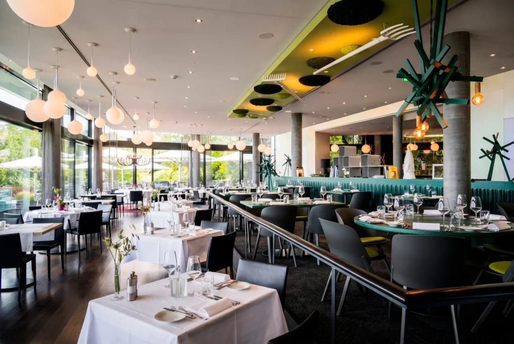 Belvoir Restaurant & Grill – lichtdurchfluteter Speisesaal mit bodentiefen Fenstern, Designer-Kugelleuchten und grünen Akzenten, gehobenes Restaurant bei Zürich, Restaurant-Transfer ab Zürich mit Chauffeur