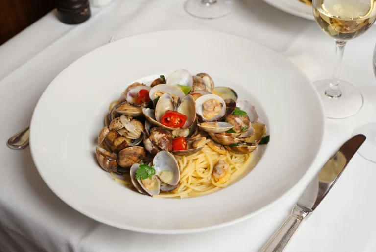 Cantinetta Antinori ab Zürich mit Chauffeur – ein Teller Spaghetti alle vongole mit frischen Venusmuscheln, Petersilie und roten Chilischeiben, dazu ein Glas Weisswein auf weiss gedecktem Tisch