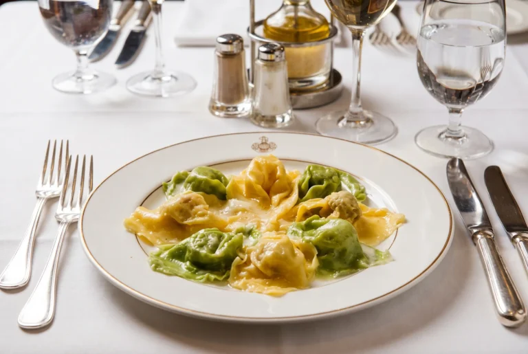 Casa Ferlin ab Zürich mit Chauffeur – der berühmte Agnolotti-Teller mit grün und gelb gefüllten Pastakissen in Butter auf einem weissen Teller mit goldenem Wappenrand, dazu Weisswein und Wasser