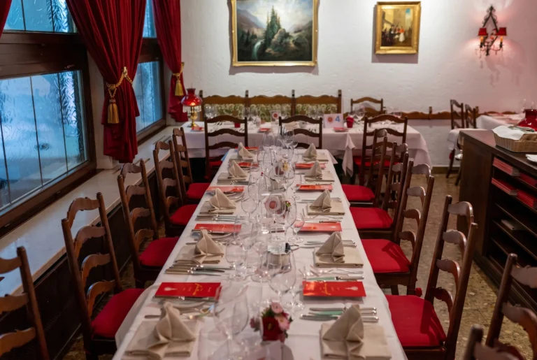 Casa Ferlin ab Zürich mit Chauffeur – der historische Speisesaal mit roten Samtvorhängen, geschnitzten Holzstühlen mit roten Sitzkissen, einer langen weiss eingedeckten Tafel und einem gerahmten Alpengemälde an der Wand