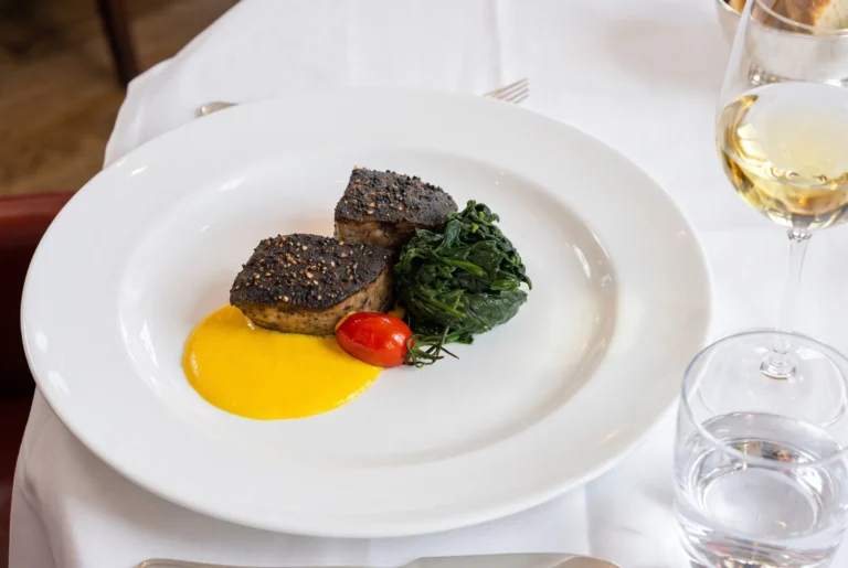 Ristorante Bianchi ab Zürich mit Chauffeur – zwei pfefferkrustierte Thunfisch-Medaillons an safrangelber Sauce mit gedünstetem Spinat und einer confierten Kirschtomate auf weissem Teller, dazu ein Glas Weisswein