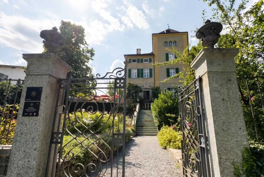 Schloss Schauenstein in Fürstenau – schmiedeeisernes Tor mit Blick auf das gelbe Schloss mit grünen Fensterläden und Rosengarten, Fine-Dining Restaurant von Andreas Caminada in Graubünden, Restaurant-Transfer ab Zürich mit Chauffeur