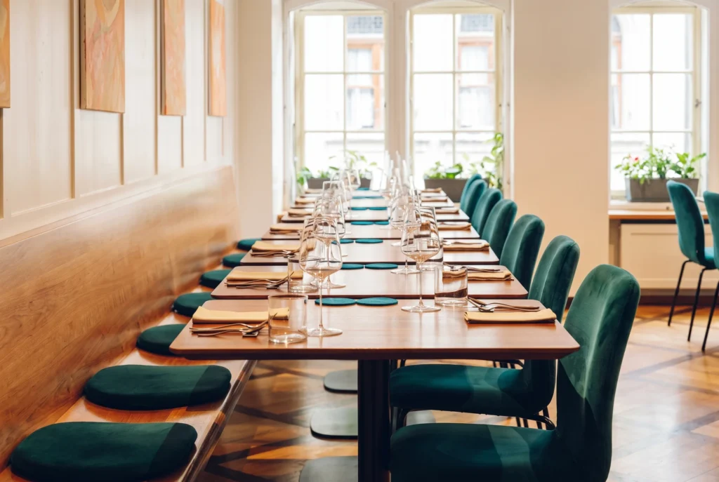 Restaurant ZOE in der Berner Altstadt – helles Interieur mit langer Holztafel, grünen Samtstühlen und Rundbogenfenstern an der Münstergasse, Fine-Dining Restaurant in Bern, Restaurant-Transfer ab Zürich mit Chauffeur